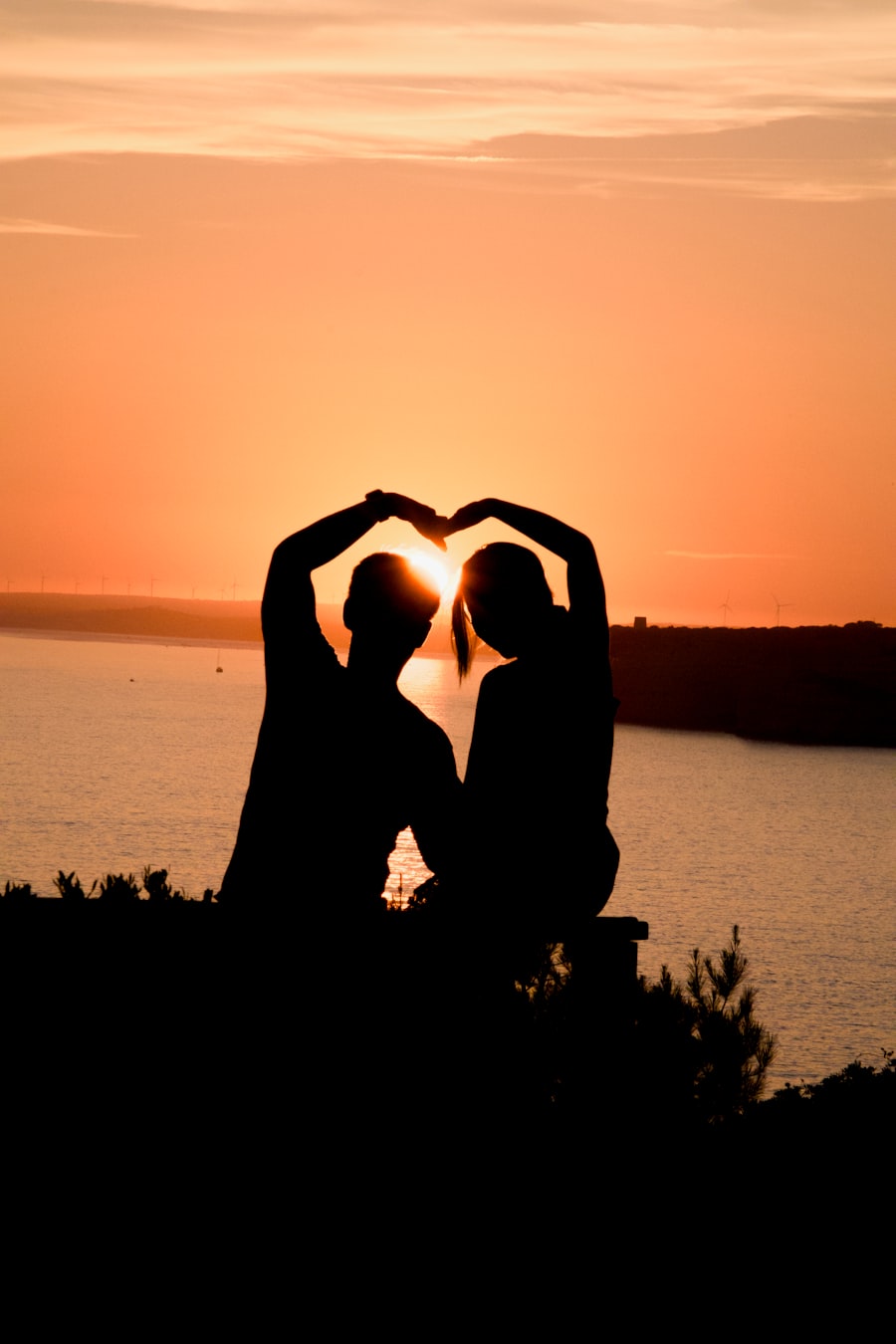 Duas pessoas formam um coração com as mãos ao pôr do sol