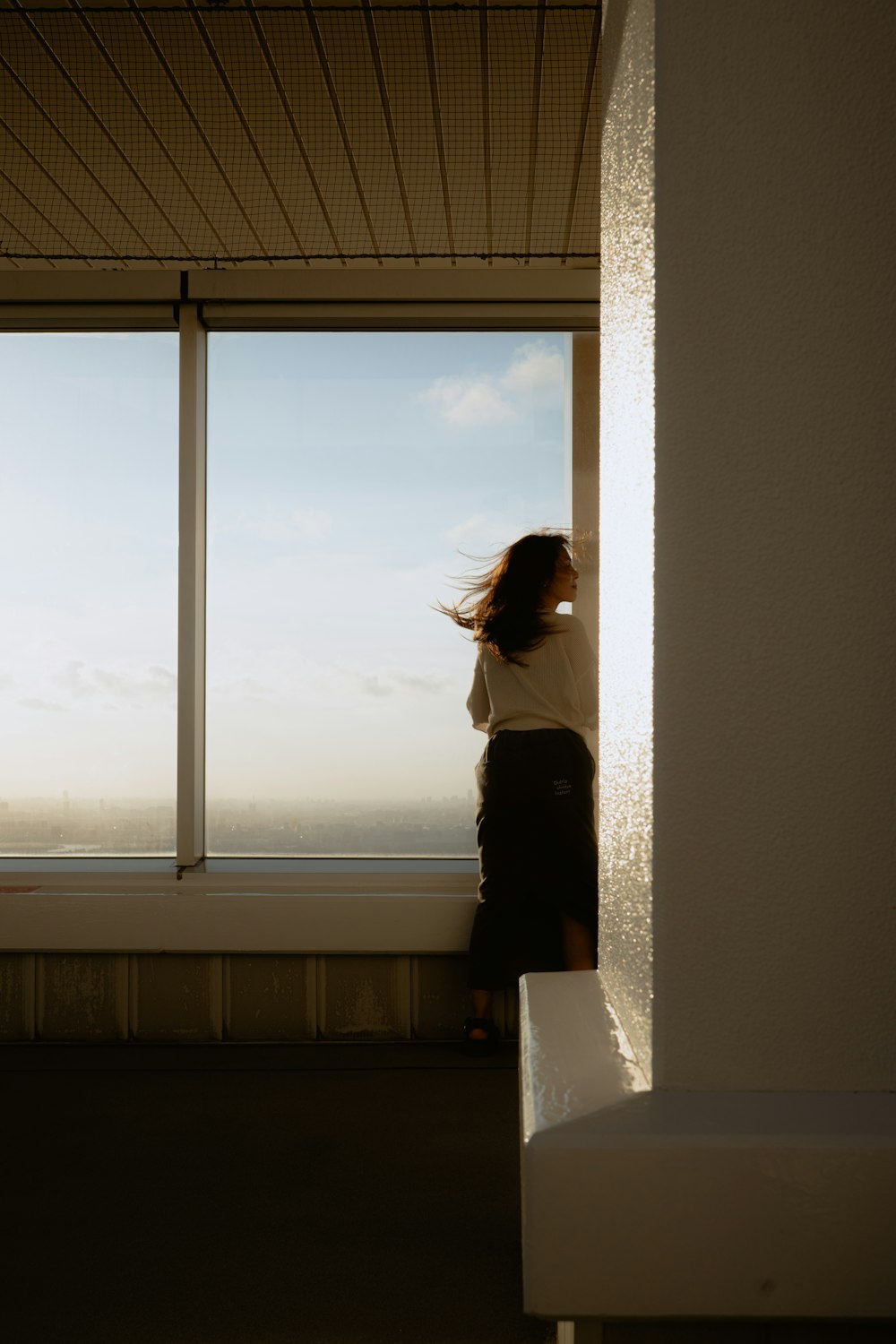 Mulher a olhar pela janela ao entardecer, num momento de introspeção